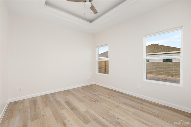 unfurnished room with a raised ceiling, light hardwood / wood-style flooring, a wealth of natural light, and ceiling fan