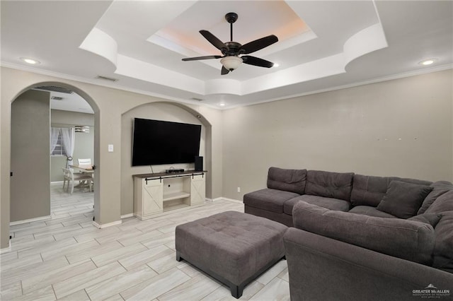 living area with baseboards, visible vents, arched walkways, a raised ceiling, and a ceiling fan