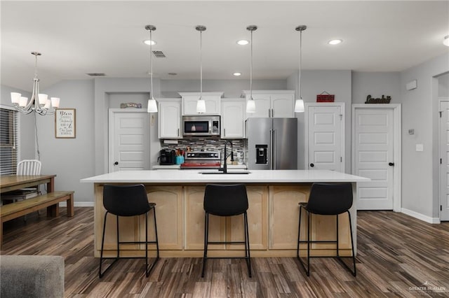 kitchen with appliances with stainless steel finishes, white cabinetry, a kitchen bar, hanging light fixtures, and a kitchen island with sink