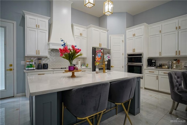 kitchen with pendant lighting, premium range hood, a kitchen breakfast bar, white cabinetry, and stainless steel appliances