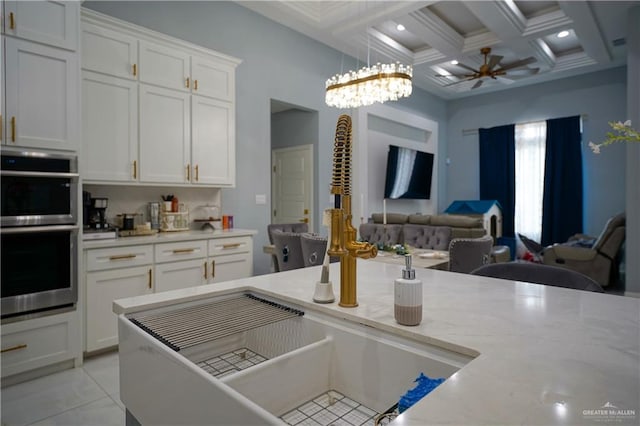 kitchen featuring coffered ceiling, light stone countertops, double oven, beamed ceiling, and white cabinetry