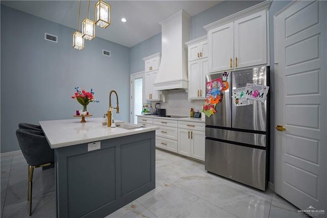 kitchen featuring stainless steel fridge, premium range hood, white cabinetry, and an island with sink