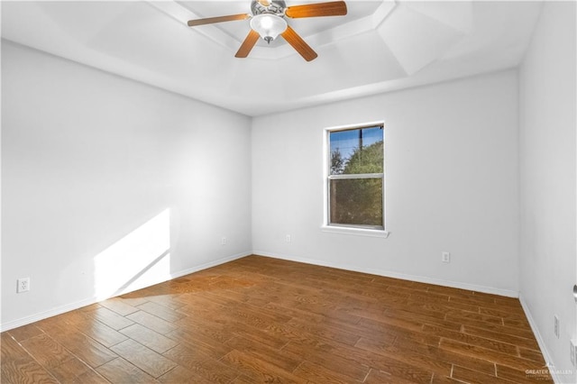 spare room with a raised ceiling, ceiling fan, and dark hardwood / wood-style flooring