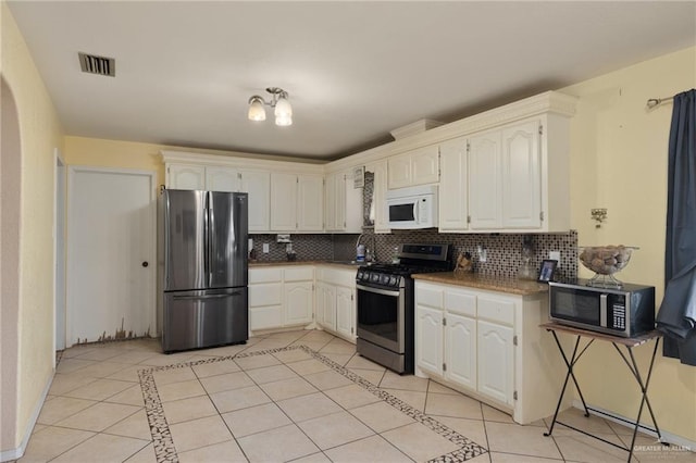 kitchen with white cabinets, light tile patterned floors, backsplash, and appliances with stainless steel finishes