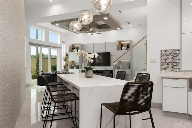 kitchen featuring decorative light fixtures, a raised ceiling, white cabinetry, and a breakfast bar area