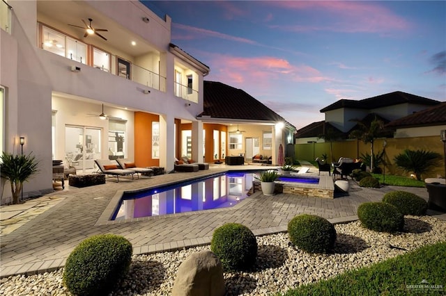 back house at dusk featuring an outdoor hangout area, a balcony, ceiling fan, and a pool with hot tub