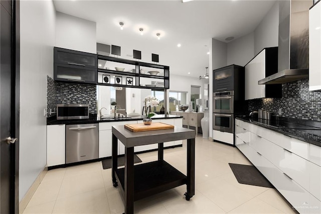 kitchen featuring light tile patterned floors, wall chimney range hood, decorative backsplash, white cabinets, and appliances with stainless steel finishes