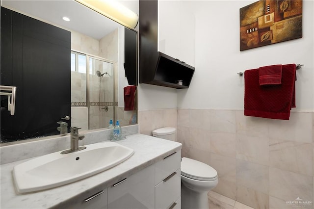 bathroom with vanity, toilet, a shower with door, and tile walls