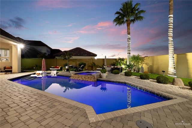 pool at dusk featuring an in ground hot tub and a patio