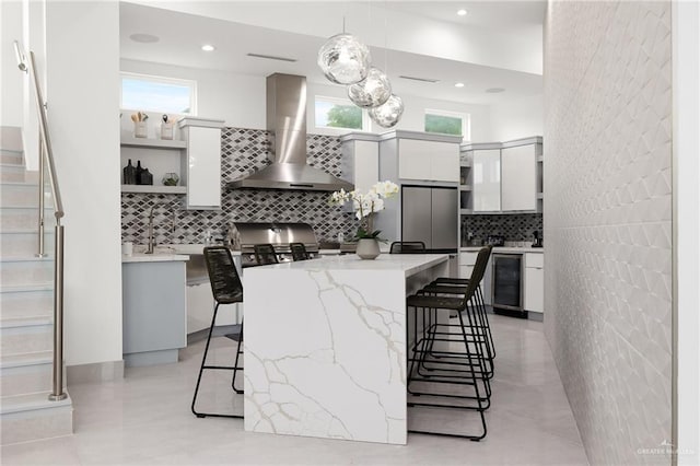 kitchen with white cabinetry, wall chimney exhaust hood, pendant lighting, a kitchen bar, and a kitchen island