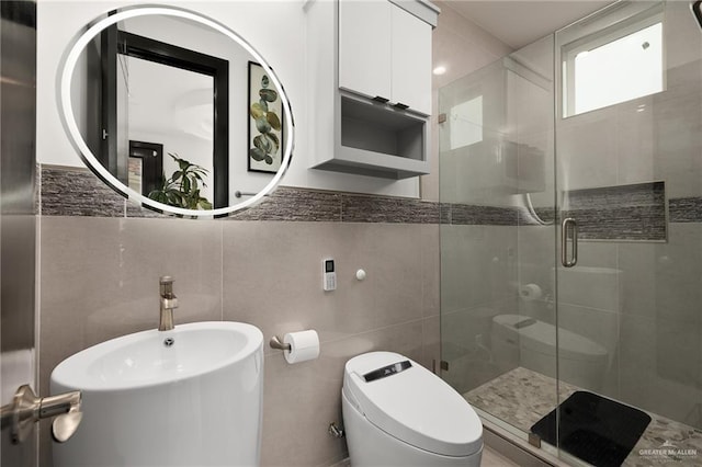 bathroom featuring sink, a shower with door, tile walls, and toilet