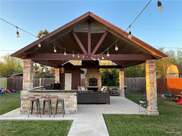 view of patio / terrace with a gazebo, an outdoor living space with a fireplace, a fenced backyard, and outdoor dry bar