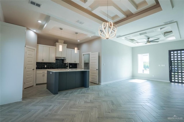 kitchen featuring white cabinetry, backsplash, an island with sink, pendant lighting, and ceiling fan with notable chandelier