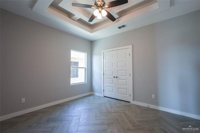 unfurnished bedroom featuring a tray ceiling, ceiling fan, a closet, and parquet floors