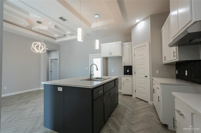 kitchen featuring white cabinets, decorative light fixtures, a raised ceiling, and an island with sink