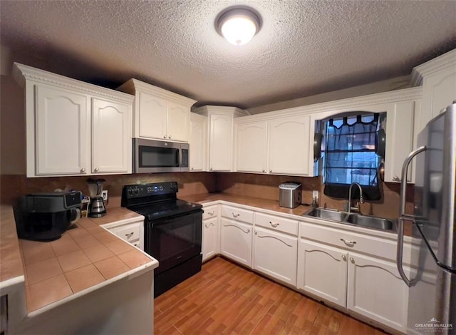 kitchen featuring sink, white cabinetry, stainless steel appliances, a textured ceiling, and light wood-type flooring