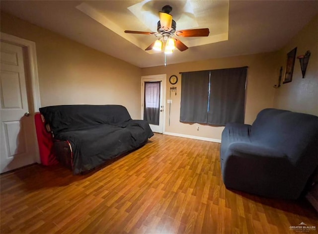 living room featuring light hardwood / wood-style flooring, a raised ceiling, and ceiling fan