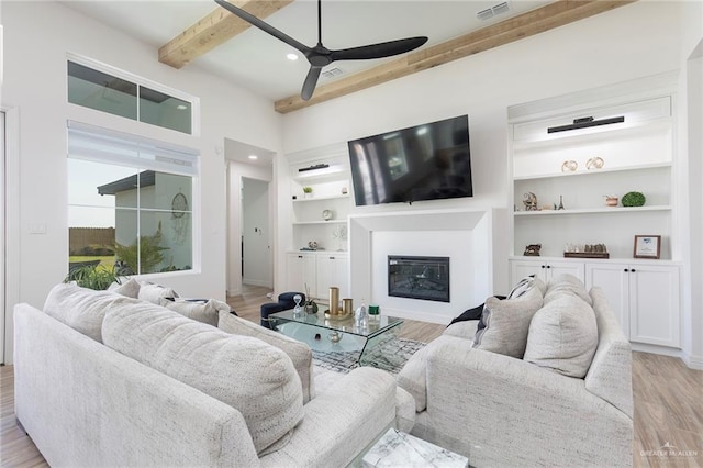 1806 E 28th St, Mission, TX 78574 - living area featuring a ceiling fan, beamed ceiling, a glass covered fireplace, light wood-style flooring, and built in shelves