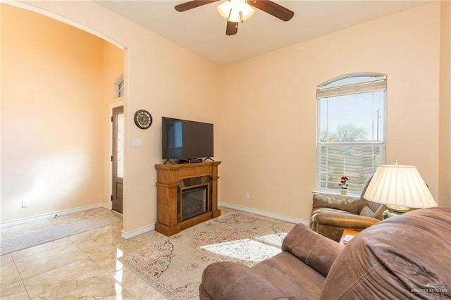 living area featuring ceiling fan, baseboards, and a glass covered fireplace