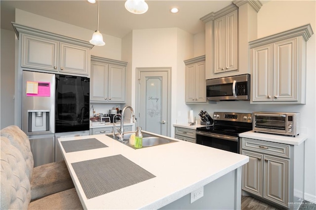 kitchen with pendant lighting, stainless steel appliances, a kitchen island with sink, and sink