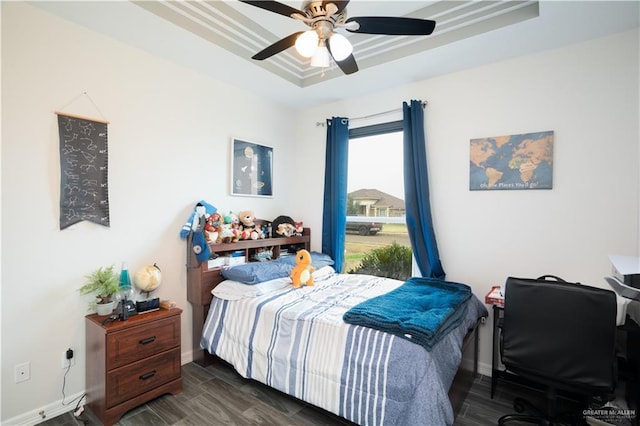 bedroom featuring dark wood-type flooring, a raised ceiling, and ceiling fan