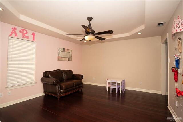 living area featuring dark hardwood / wood-style floors, ceiling fan, and a raised ceiling