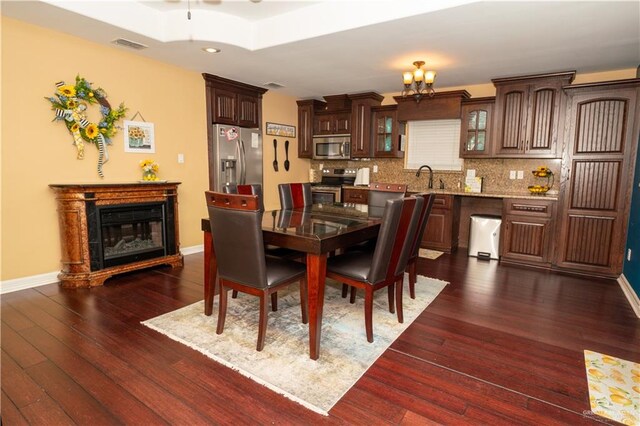 dining room featuring a raised ceiling, sink, dark hardwood / wood-style floors, and an inviting chandelier