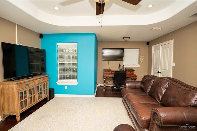 living room featuring ceiling fan, dark wood-type flooring, and a tray ceiling