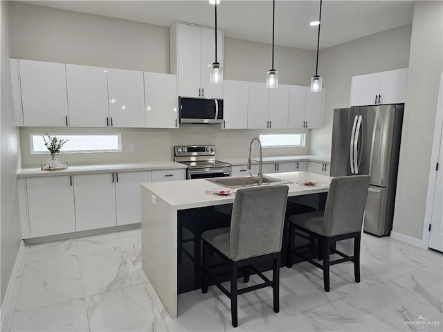 kitchen with sink, white cabinetry, stainless steel appliances, an island with sink, and decorative light fixtures