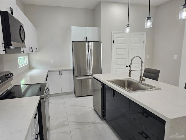 kitchen featuring pendant lighting, sink, appliances with stainless steel finishes, white cabinetry, and an island with sink