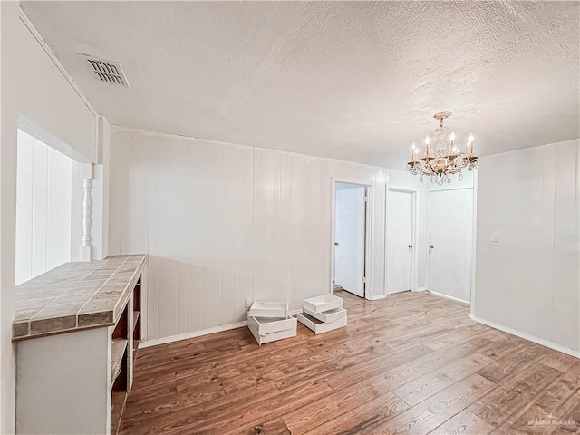 spare room with a textured ceiling, hardwood / wood-style flooring, and a notable chandelier