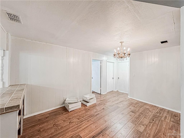 unfurnished room featuring hardwood / wood-style flooring, a notable chandelier, a textured ceiling, and wooden walls