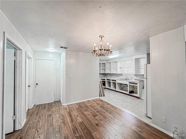 interior space featuring an inviting chandelier, sink, a textured ceiling, and light hardwood / wood-style flooring