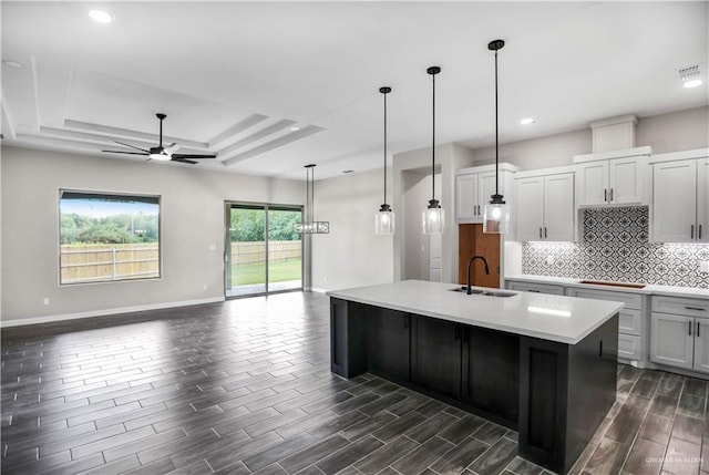 kitchen with ceiling fan, a raised ceiling, black cooktop, pendant lighting, and a center island with sink