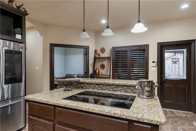 kitchen featuring stainless steel refrigerator, light stone counters, decorative light fixtures, black electric cooktop, and dark brown cabinets