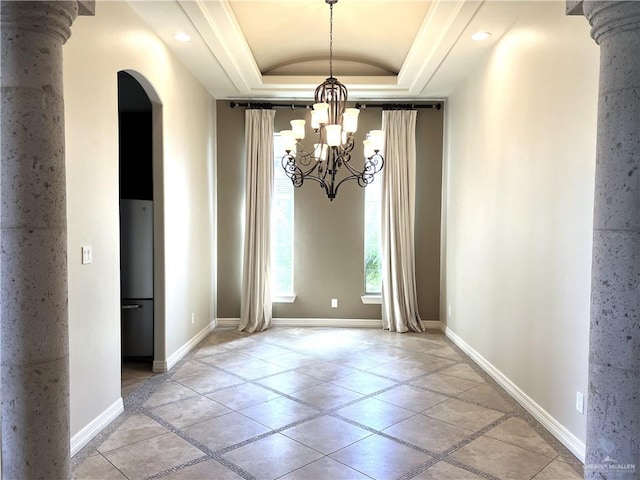 unfurnished dining area with a tray ceiling, ornate columns, light tile patterned floors, and an inviting chandelier