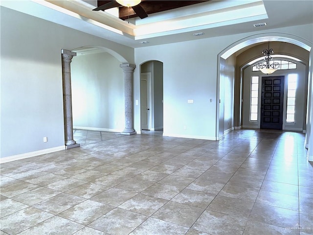 unfurnished room with a raised ceiling, ceiling fan with notable chandelier, and ornate columns