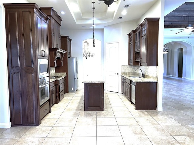 kitchen with dark brown cabinetry, sink, a tray ceiling, decorative backsplash, and appliances with stainless steel finishes