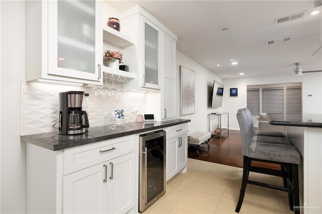 kitchen with light tile patterned flooring, white cabinetry, wine cooler, backsplash, and dark stone counters