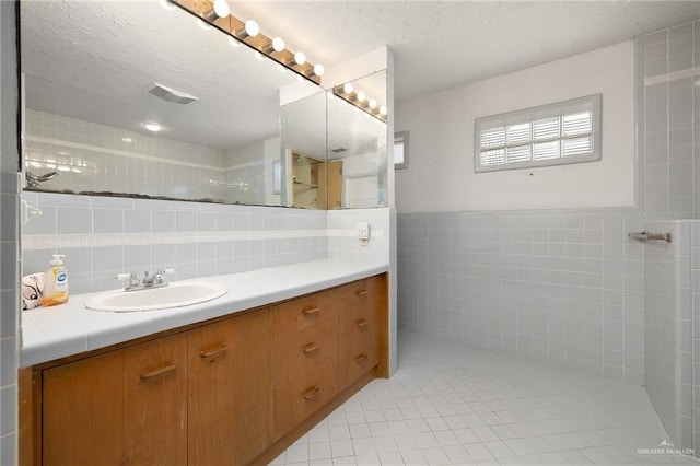 bathroom with tile walls, vanity, tile patterned floors, and a textured ceiling