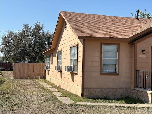 view of home's exterior with cooling unit, roof with shingles, and fence