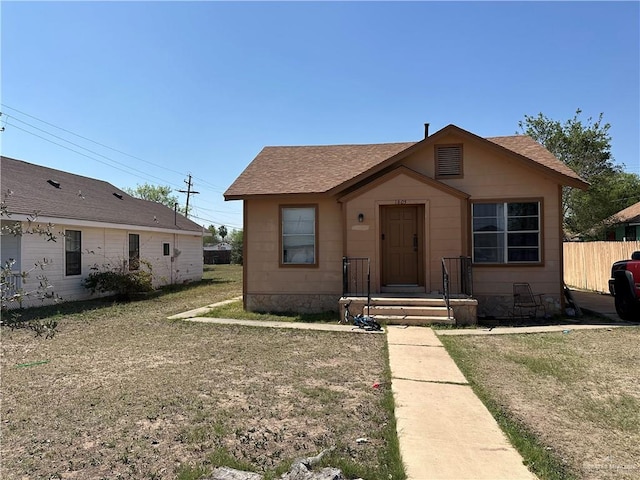 bungalow-style home with a shingled roof and fence