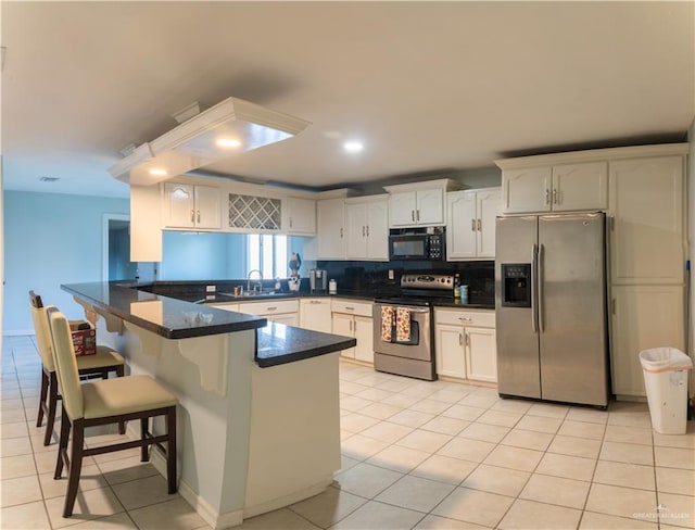 kitchen with a breakfast bar area, kitchen peninsula, white cabinets, and appliances with stainless steel finishes