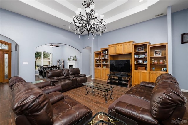 living area with arched walkways, a chandelier, a fireplace, wood finished floors, and a raised ceiling