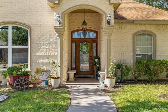 view of exterior entry featuring a shingled roof and brick siding