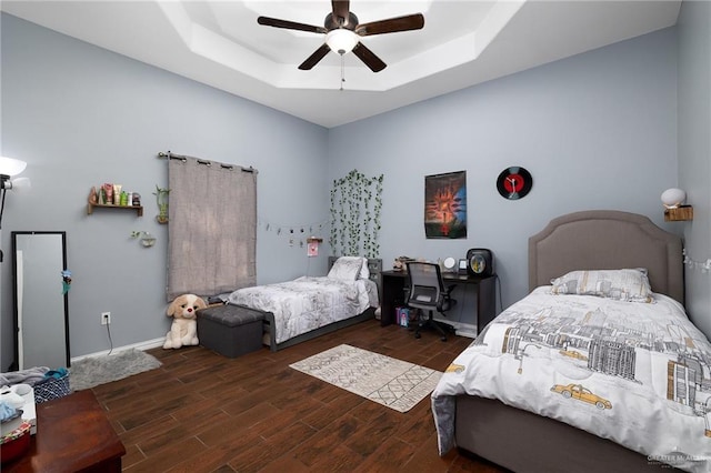 bedroom featuring baseboards, ceiling fan, a tray ceiling, and wood finished floors