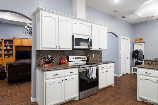 kitchen featuring arched walkways, stainless steel appliances, white cabinetry, tasteful backsplash, and dark wood finished floors