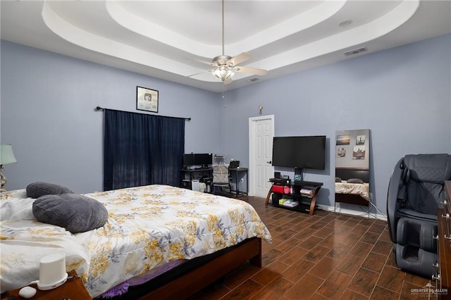 bedroom featuring visible vents, a tray ceiling, a ceiling fan, and wood finish floors