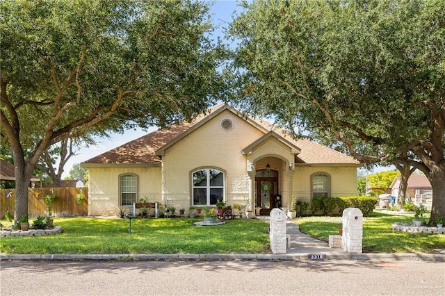 mediterranean / spanish home with a front yard, fence, and brick siding