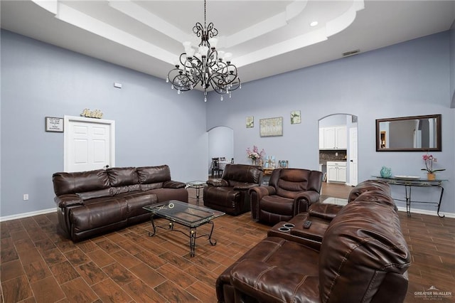 living area featuring arched walkways, wood finished floors, a raised ceiling, and an inviting chandelier